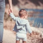 From behind view of toddler walking with parent on seashore