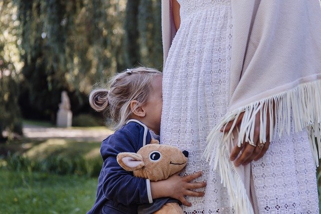 little girl hiding in woman's white skirt holding a stuffed animal