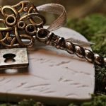 Closeup of old decorative skeleton key tied to a heart wiht ribbon and all lying on green moss