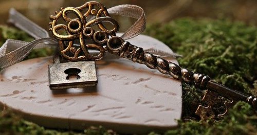 Closeup of old decorative skeleton key tied to a heart wiht ribbon and all lying on green moss